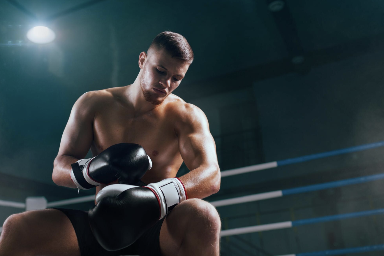 chico con traje de box sentado en el ring asegurando sus guantes boxing