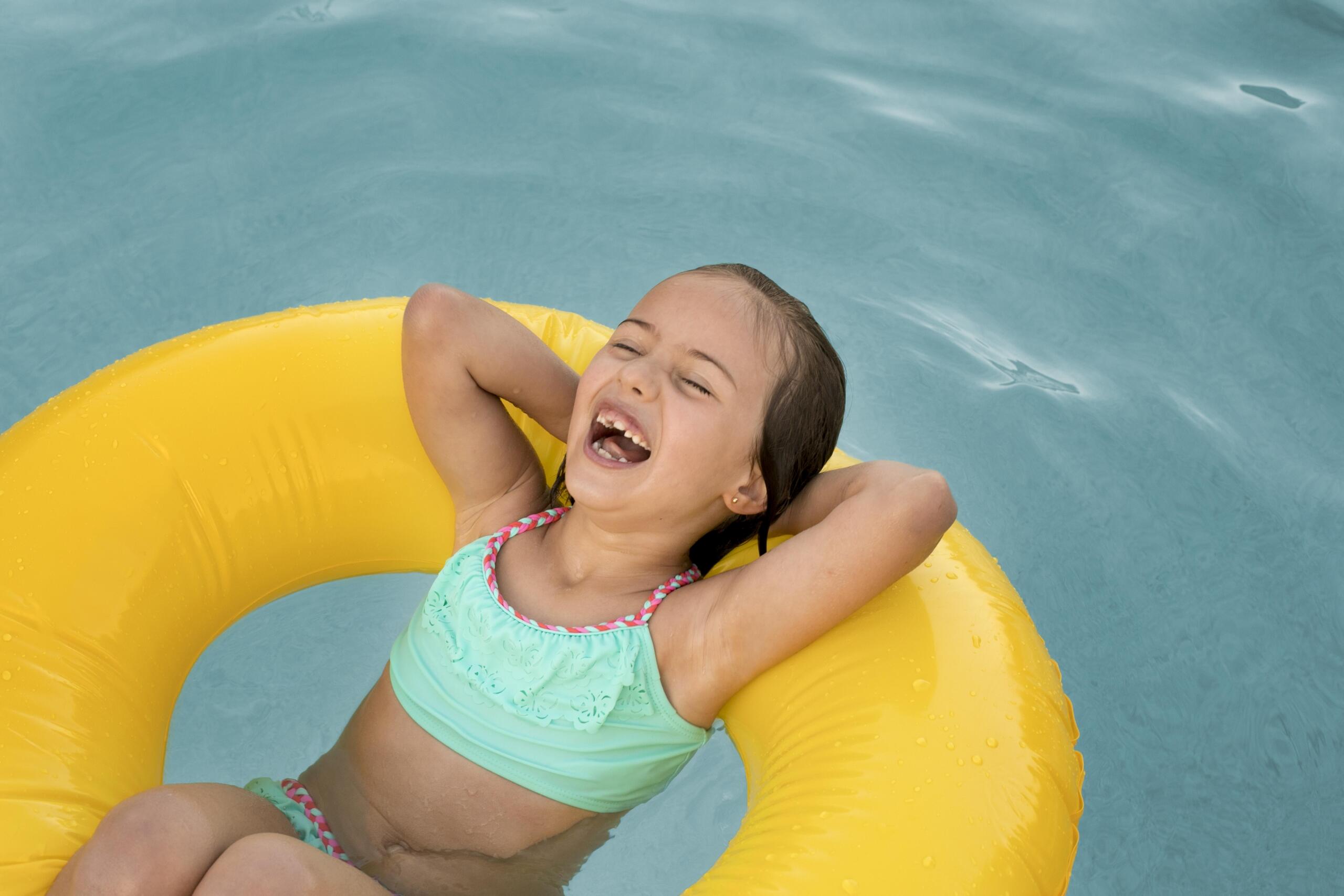 niña riendo recostada en medio de un flotador amarillo en medio de la piscina