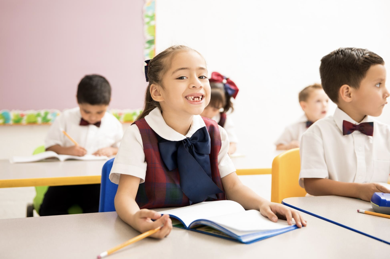 niña pequeña sonriente mirando a la cámara uniformada junto a sus compañeros de aula