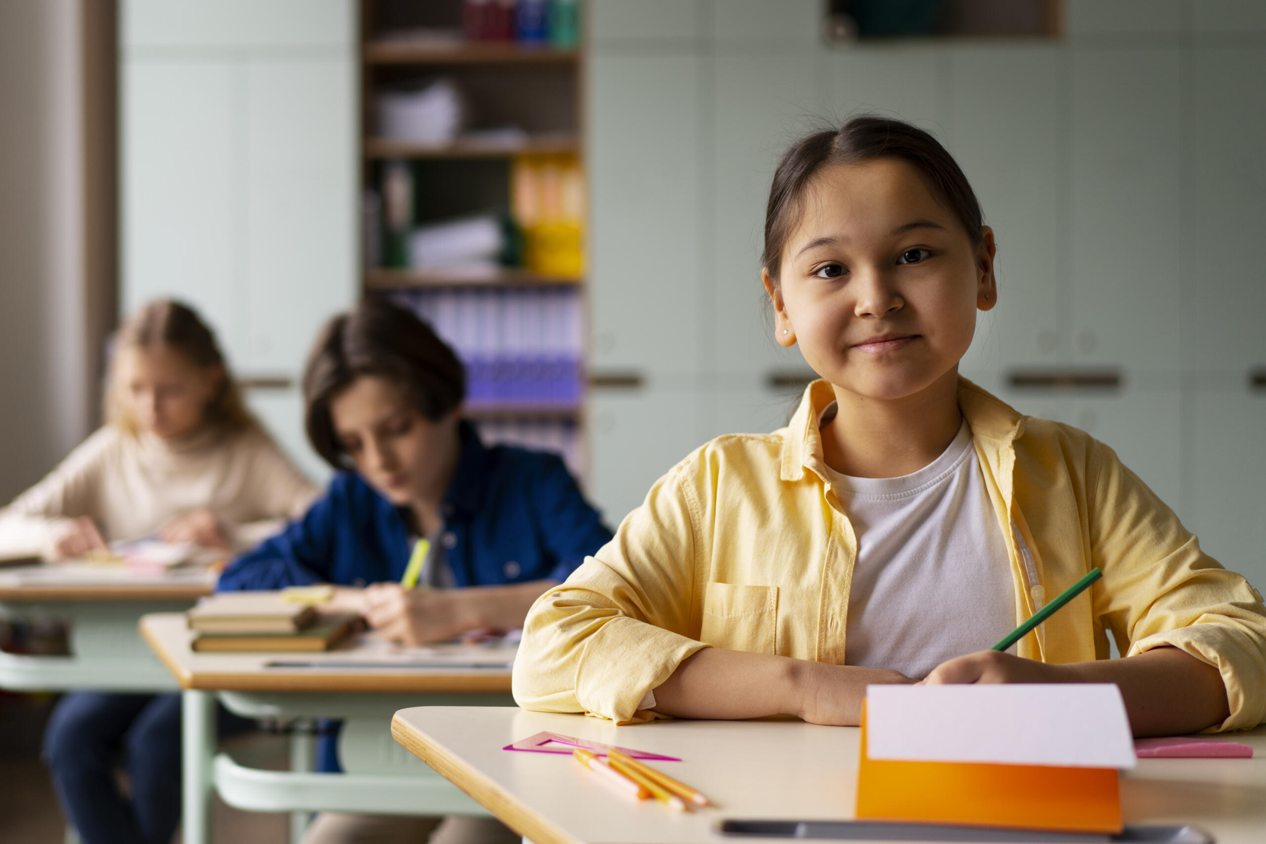 niña sonriente en su carpeta de aula llena de útiles con sus compañeros de fondo