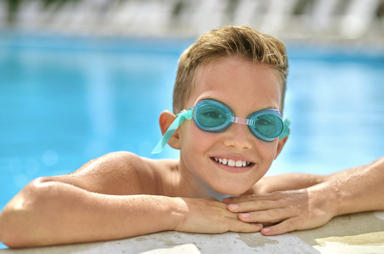 niño sonriente apoyado en el borde de la piscina recién salido de bucear con lentes de natación