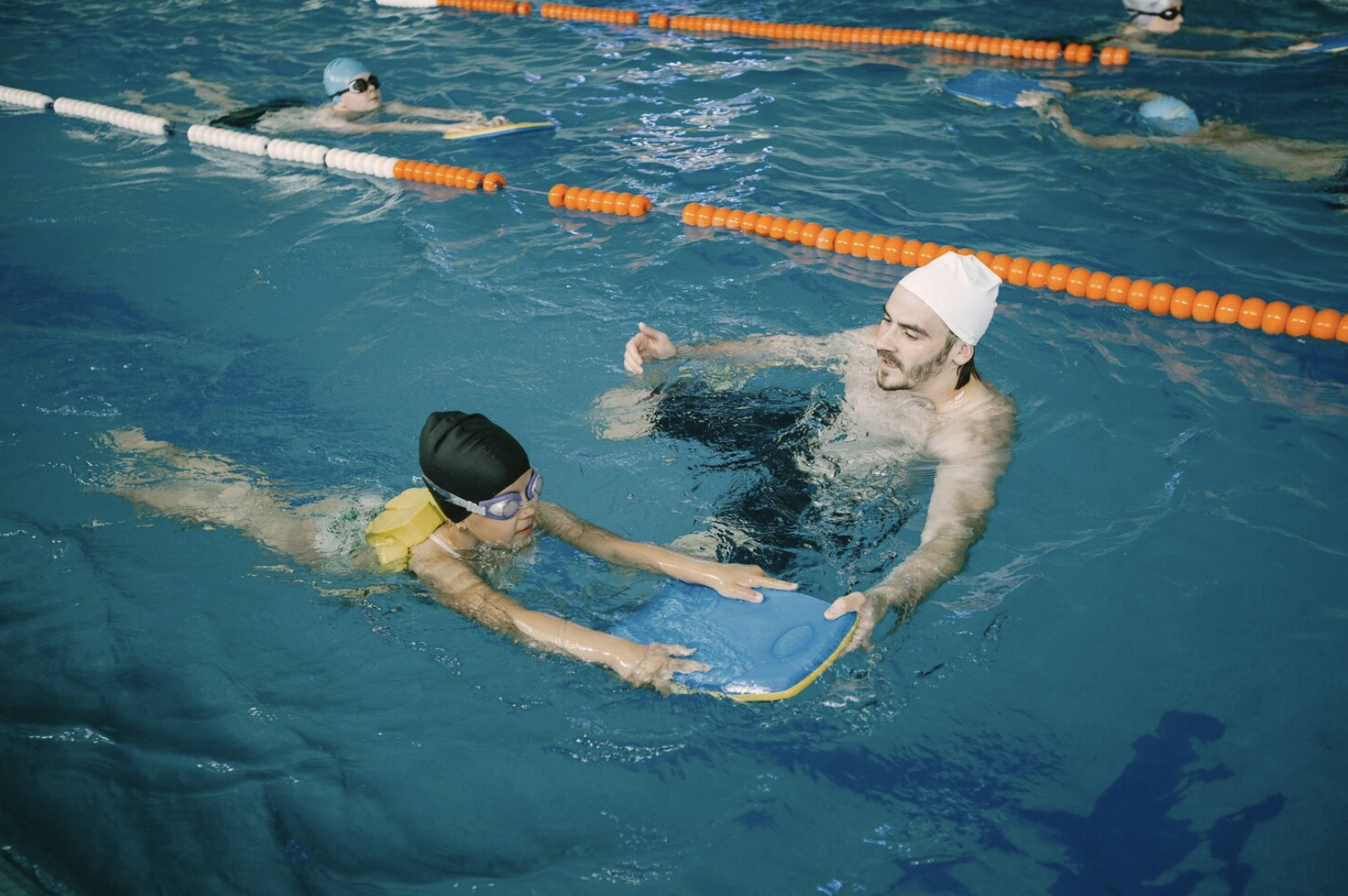 profesor de natación en la piscina que está ayudando a nadar con una tabla a un niño
