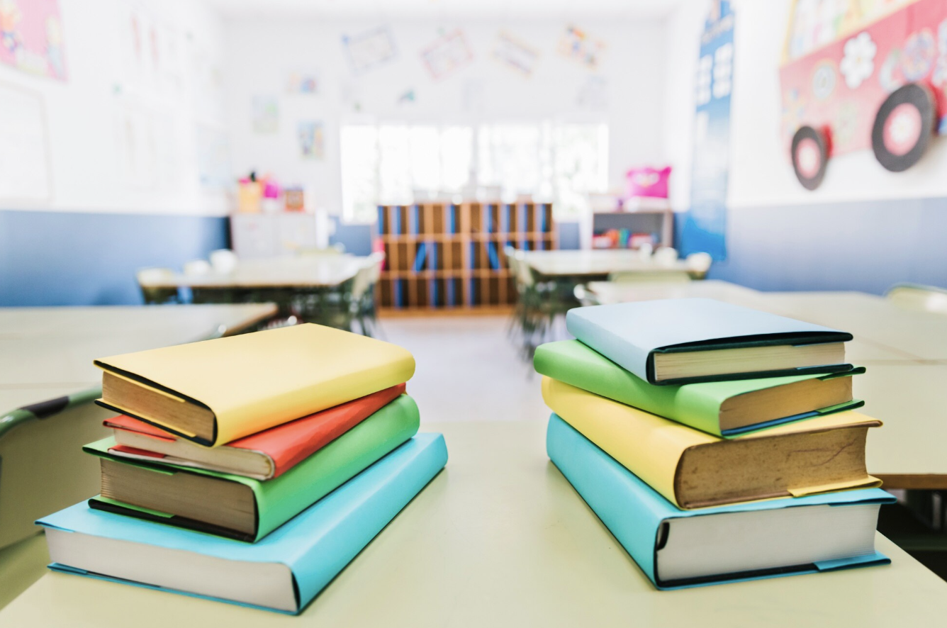 libros de colores uno sobre otro en primer plano con un aula de fondo