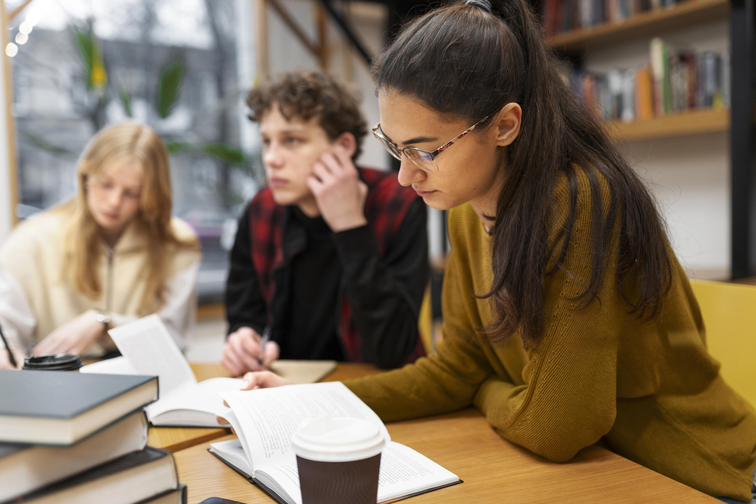 toma detalle de tres alumnos estudiando juntos con libros y cuaderno de notas sobre el escritorio.