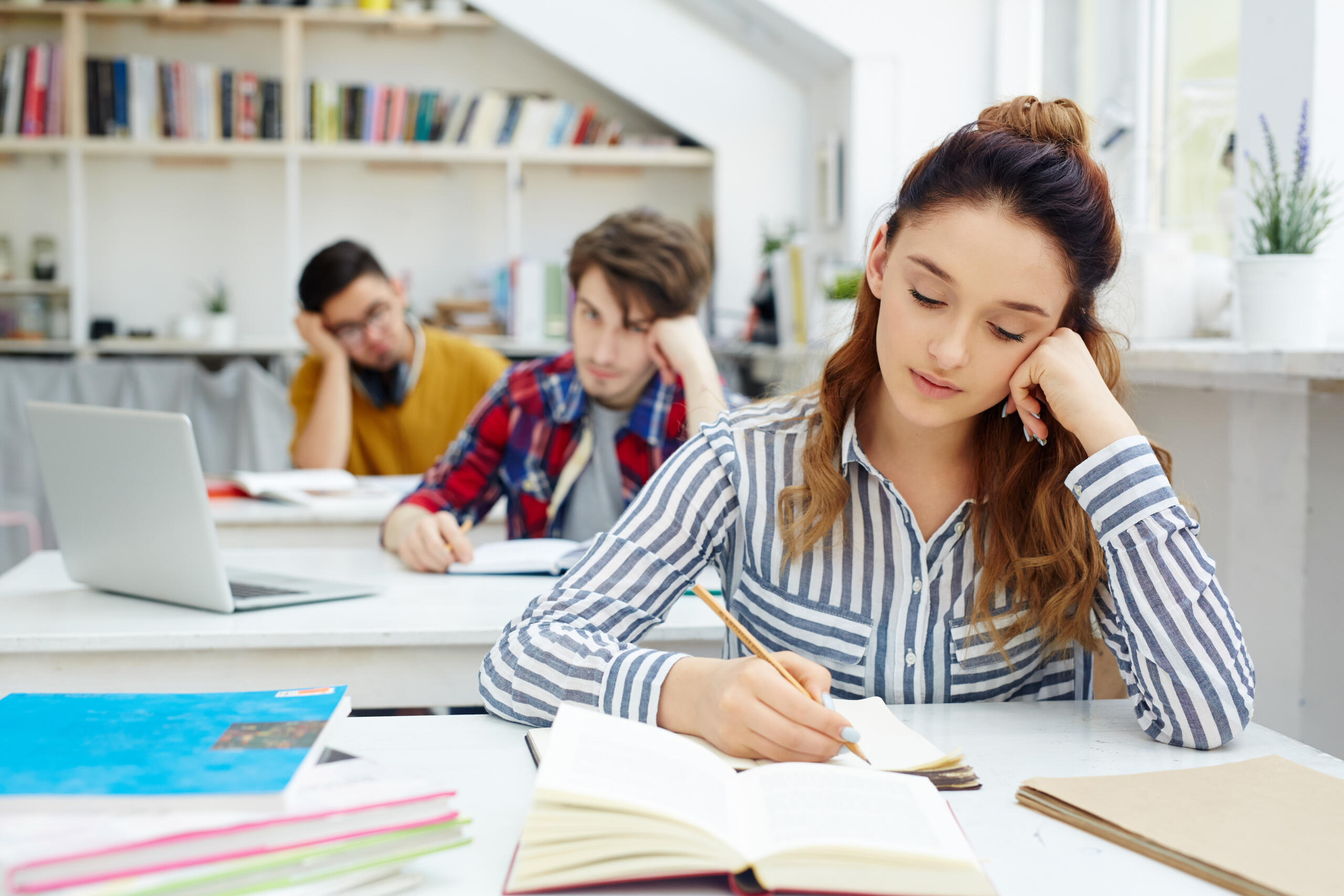 alumnos sentados en fila con escritorios individuales estudiando con una chica en primer plano