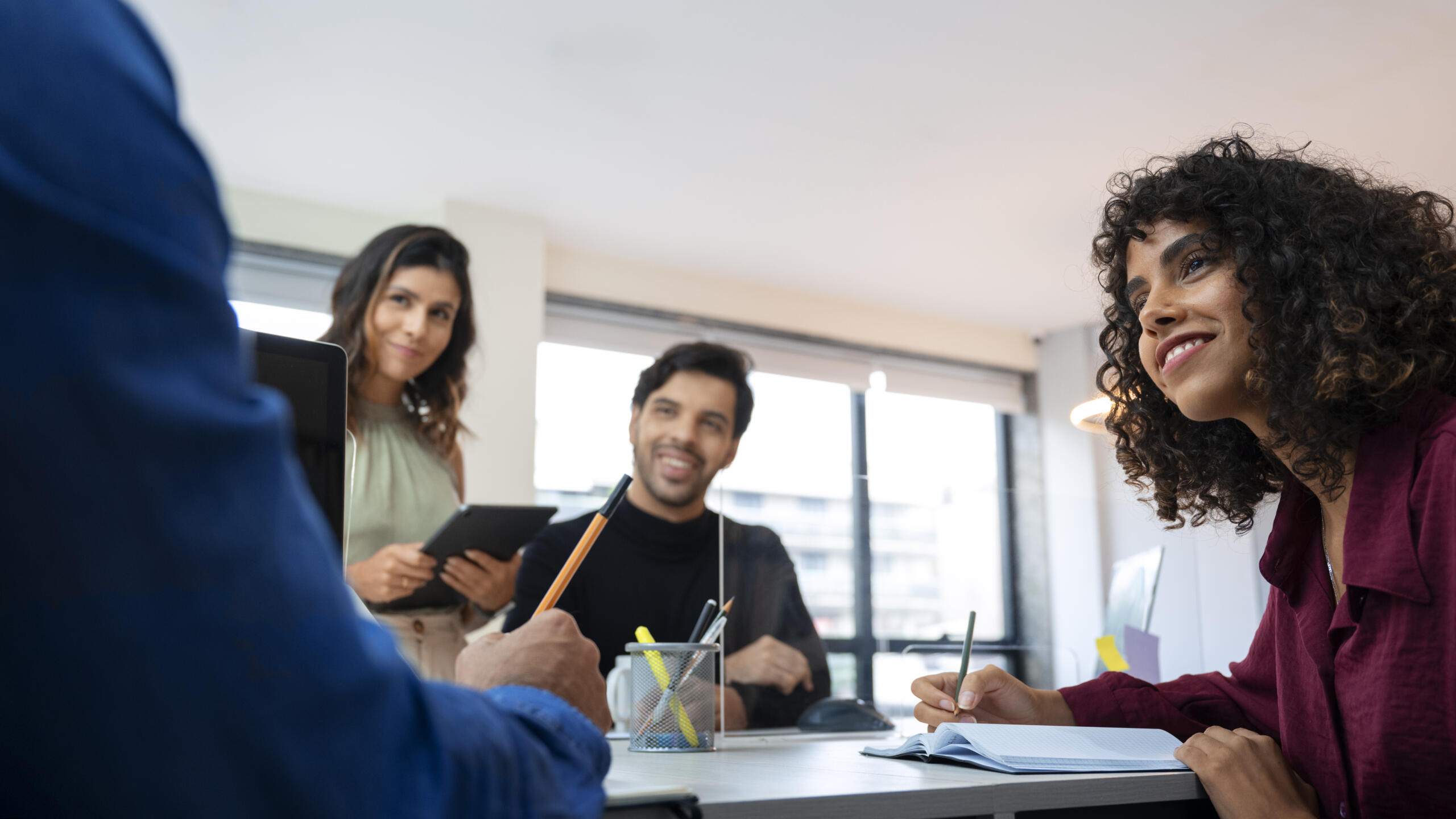 grupo de cuatro jovenes estudiando juntos en un escritorio con lápices, hojas y cuadernos esparcidos en la mesa