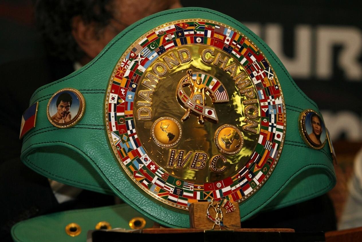Cinturón de campeón mundial de boxeo de la WBC con el centro dorado, varias banderas nacionales y retratos en una correa de cuero verde.