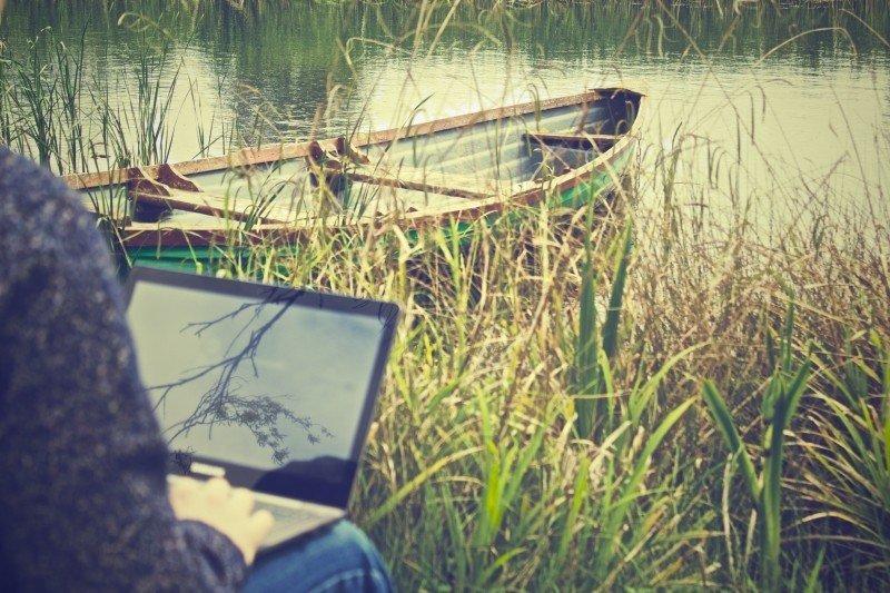 osoba siedząca z laptopem nad jeziorem