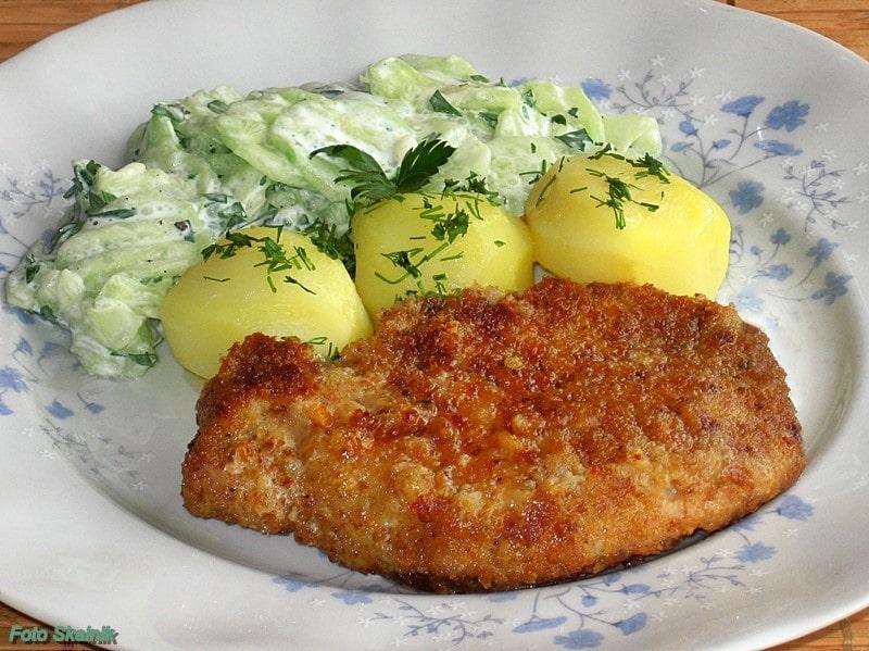 kotlet schabowy z ziemniakami posypanymi koperkiem i mizerią podane na talerzu