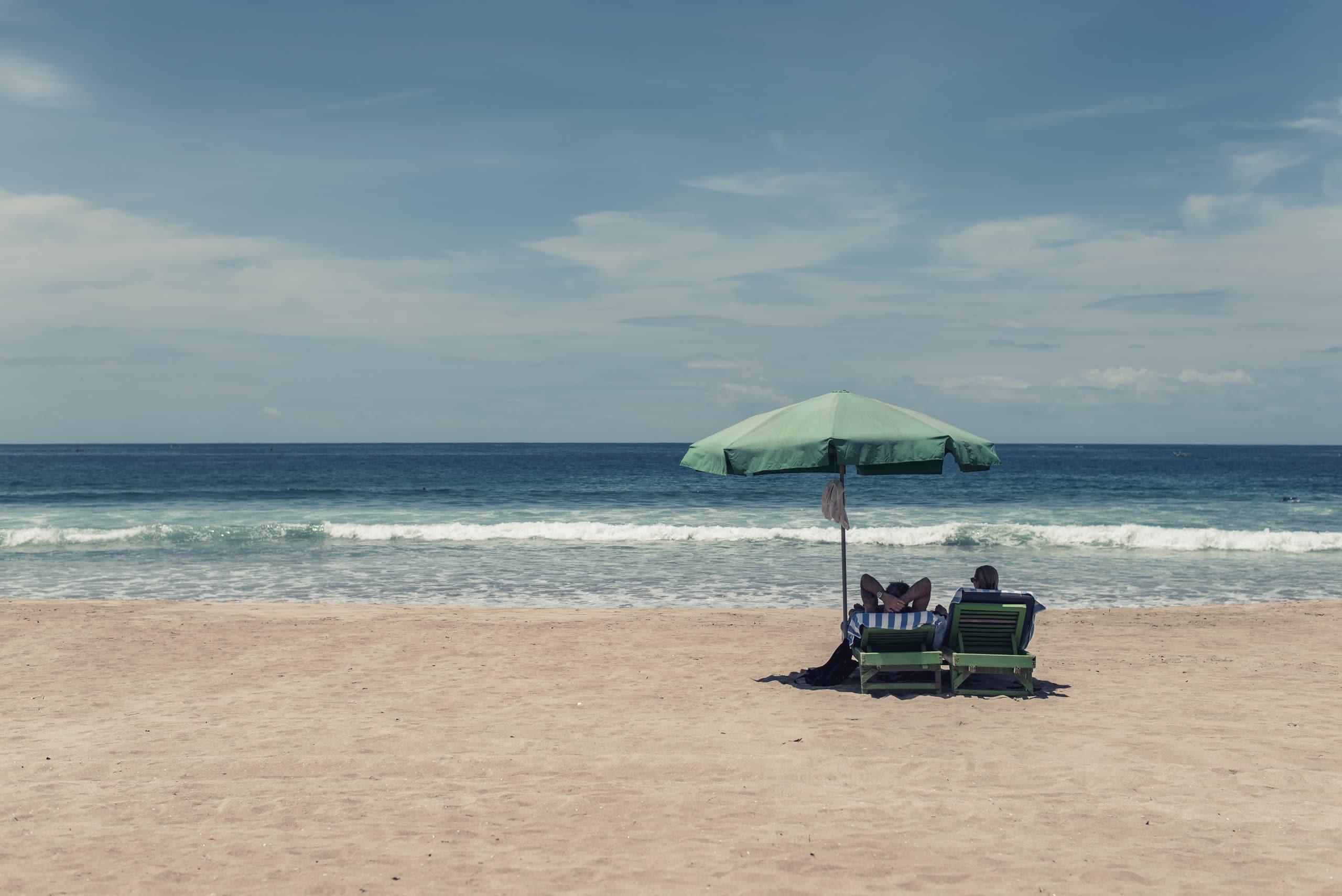 Dwa leżaki pod parasolem na plaży.