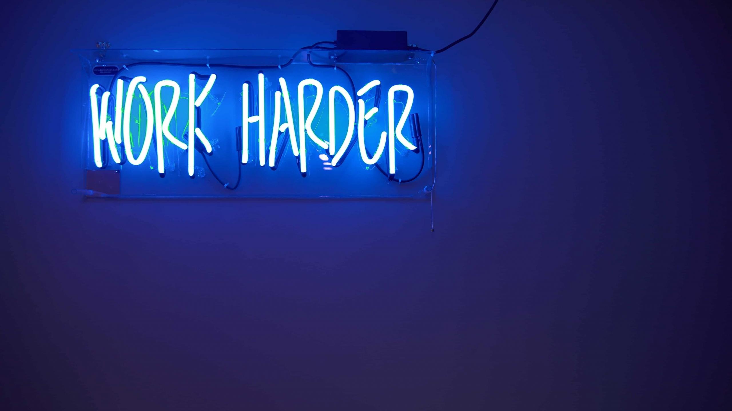 niebieski neon z napisem work harder pracuj ciężej wiszący na ścianie