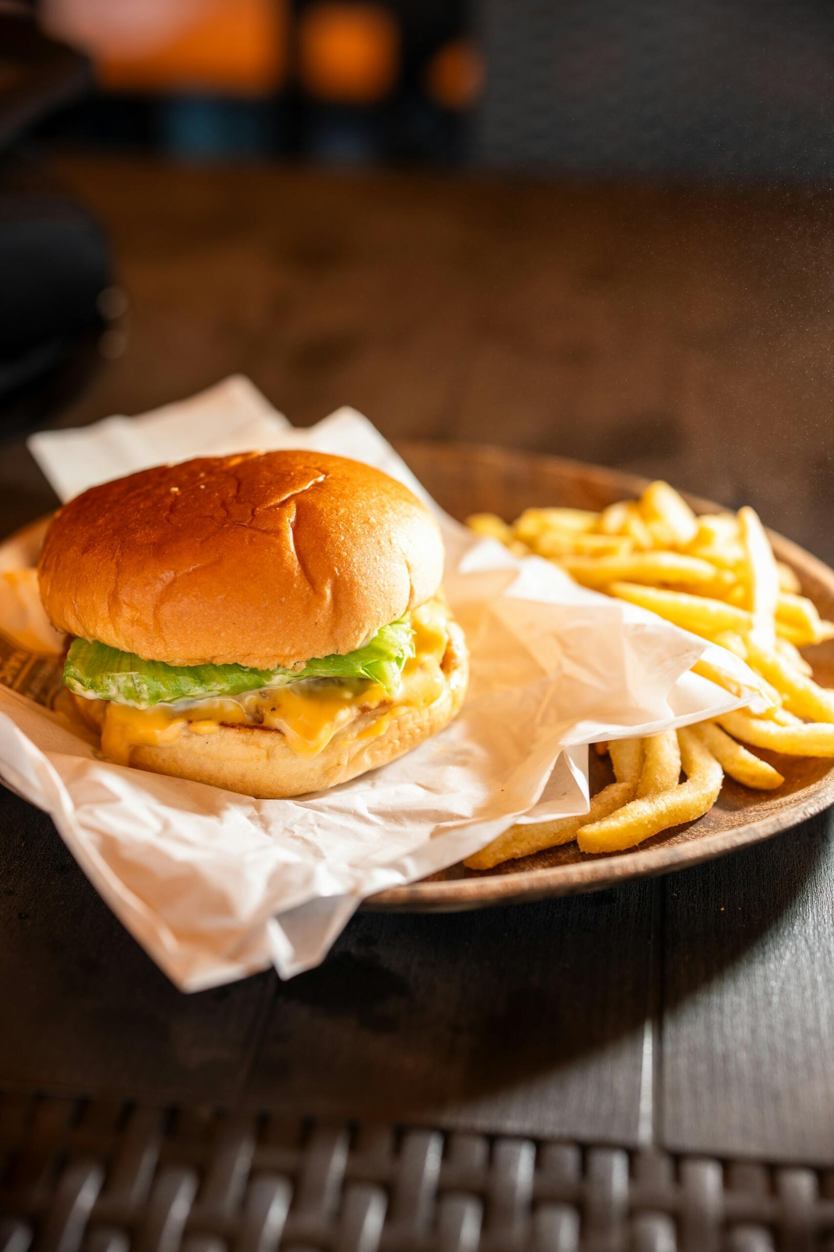 Cheeseburger z sałatą i roztopionym serem, podany wraz ze złocistymi frytkami na papierze pergaminowym.