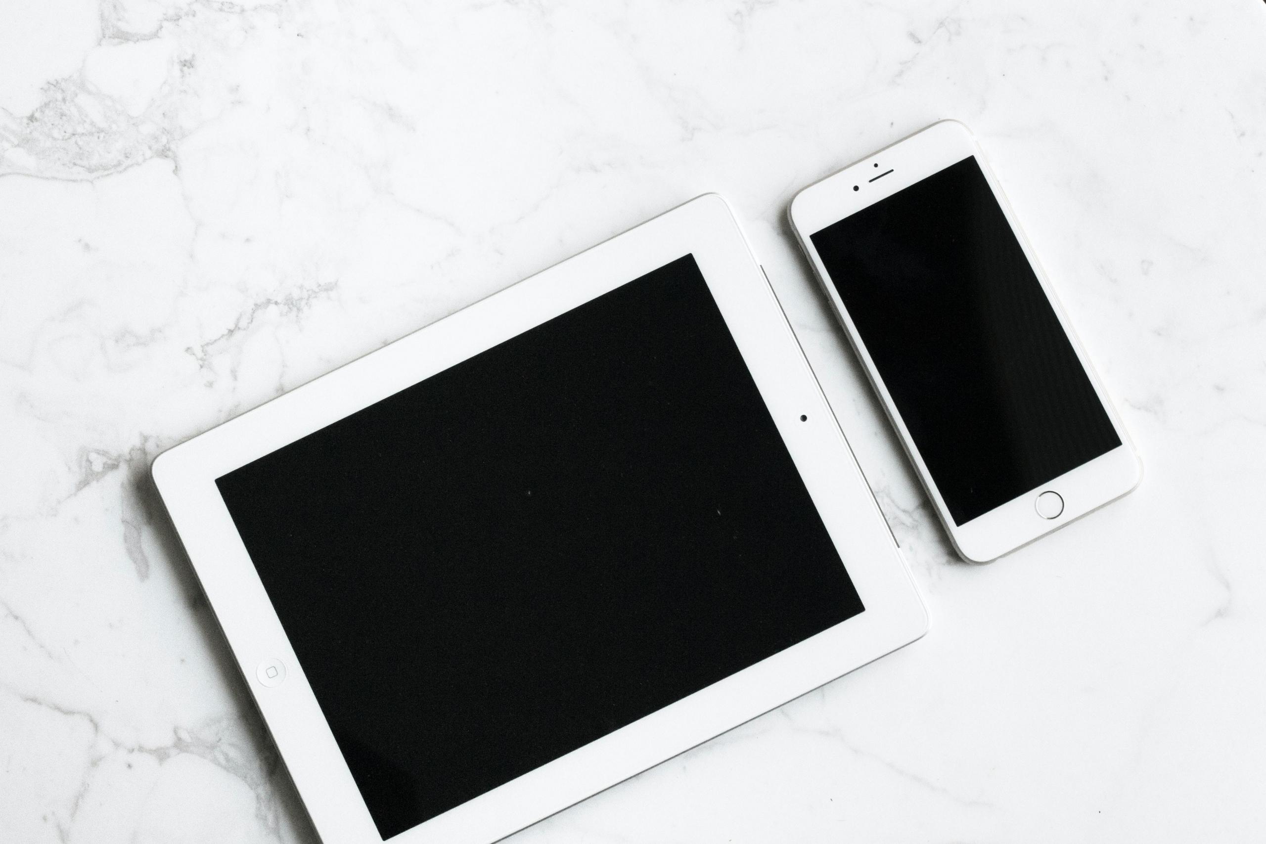biały smartfon i biały tablet leżące na marmurowym blacie