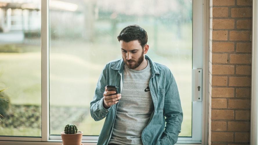 Mężczyzna z telefonem w ręku stojący przy oknie