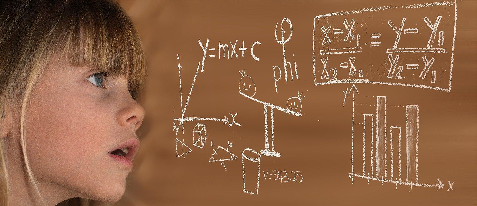 Dziewczynka patrząca na wzory matematyczne na brązowej tablicy.