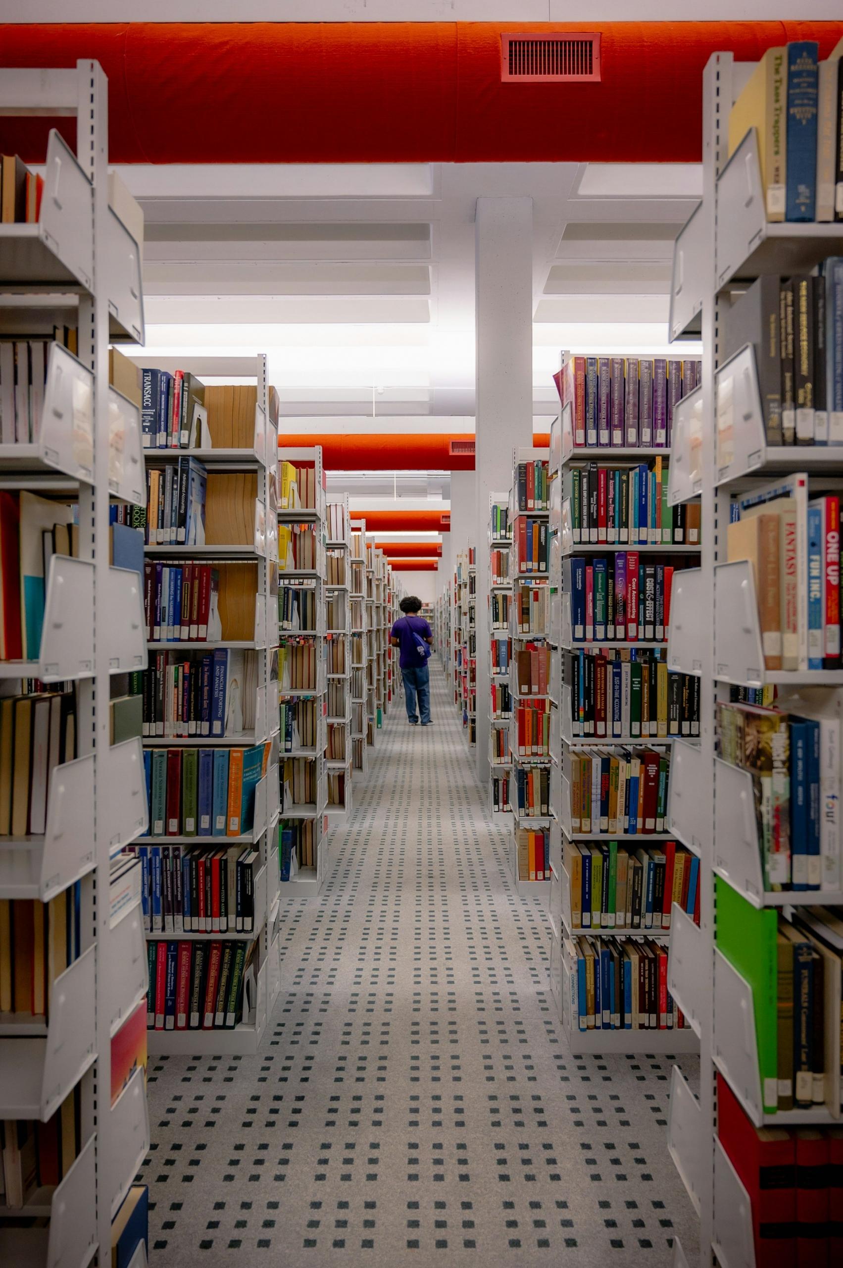 Człowiek wśród regałów z książkami w bibliotece z czerwonym sufitem.
