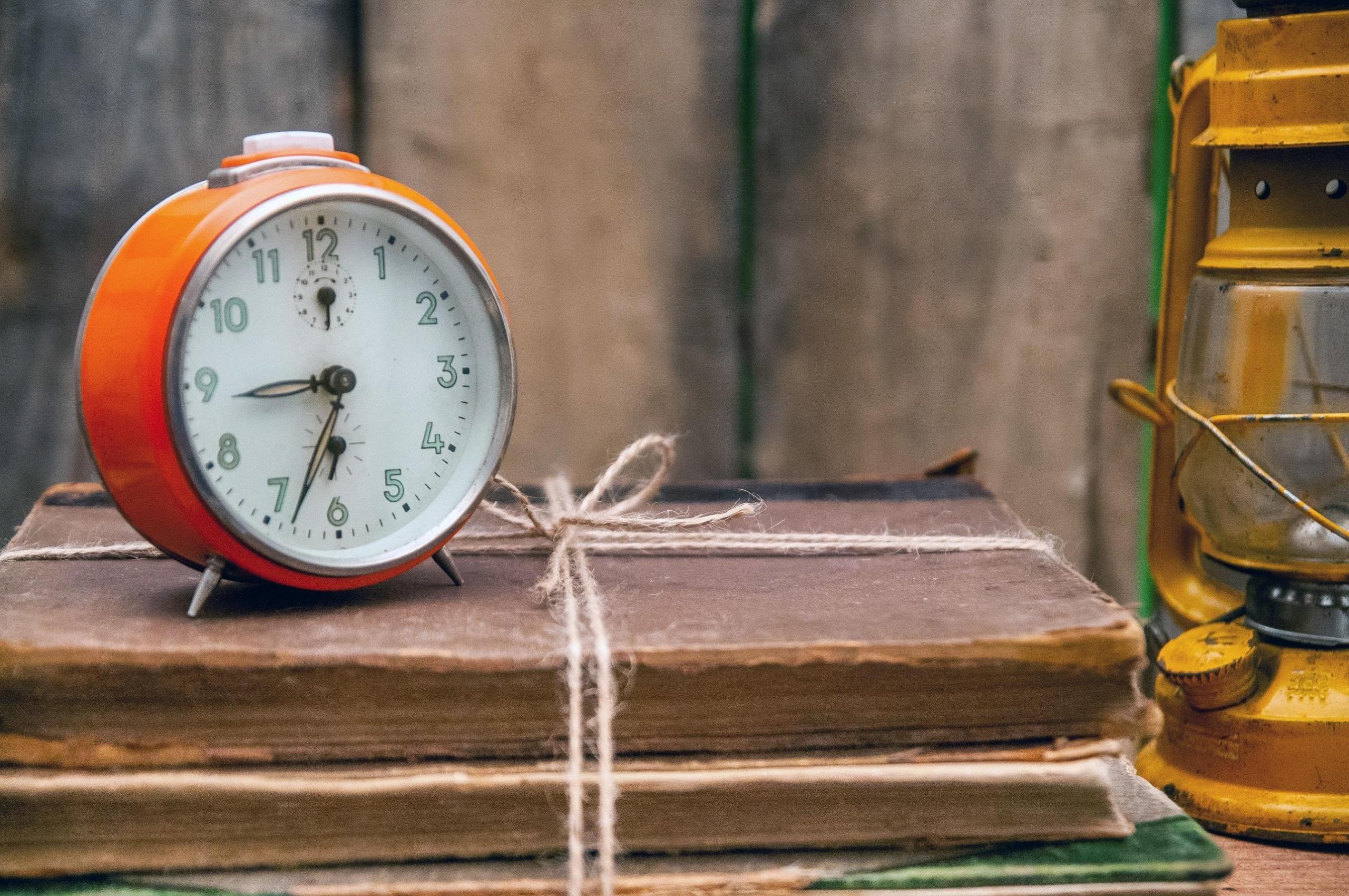 Budzik stojący na kilku książkach na biurku.