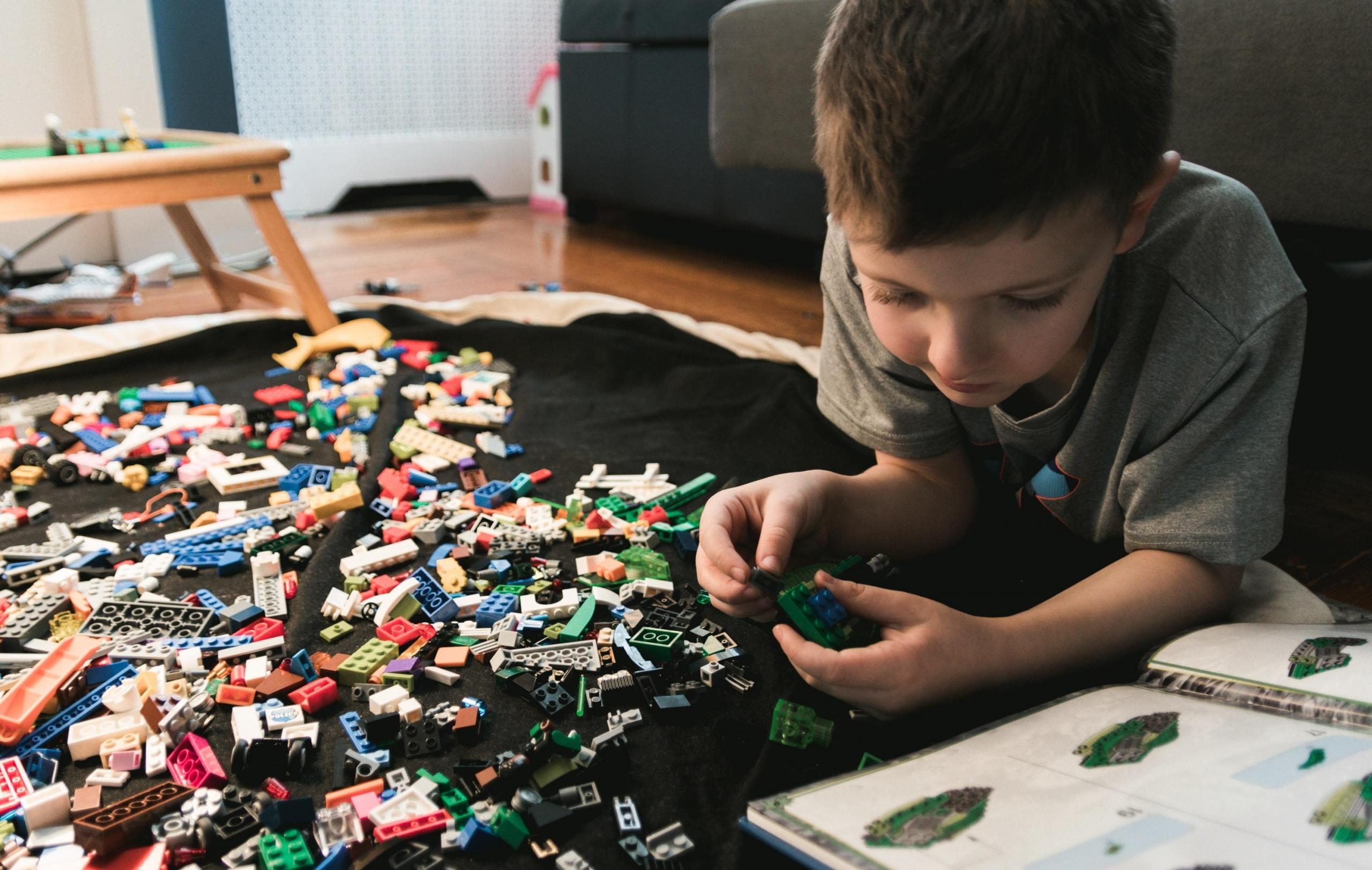 Chłopiec na podłodze, układający klocki LEGO, czarny koc, stoliczek, kanapa, grzejnik.