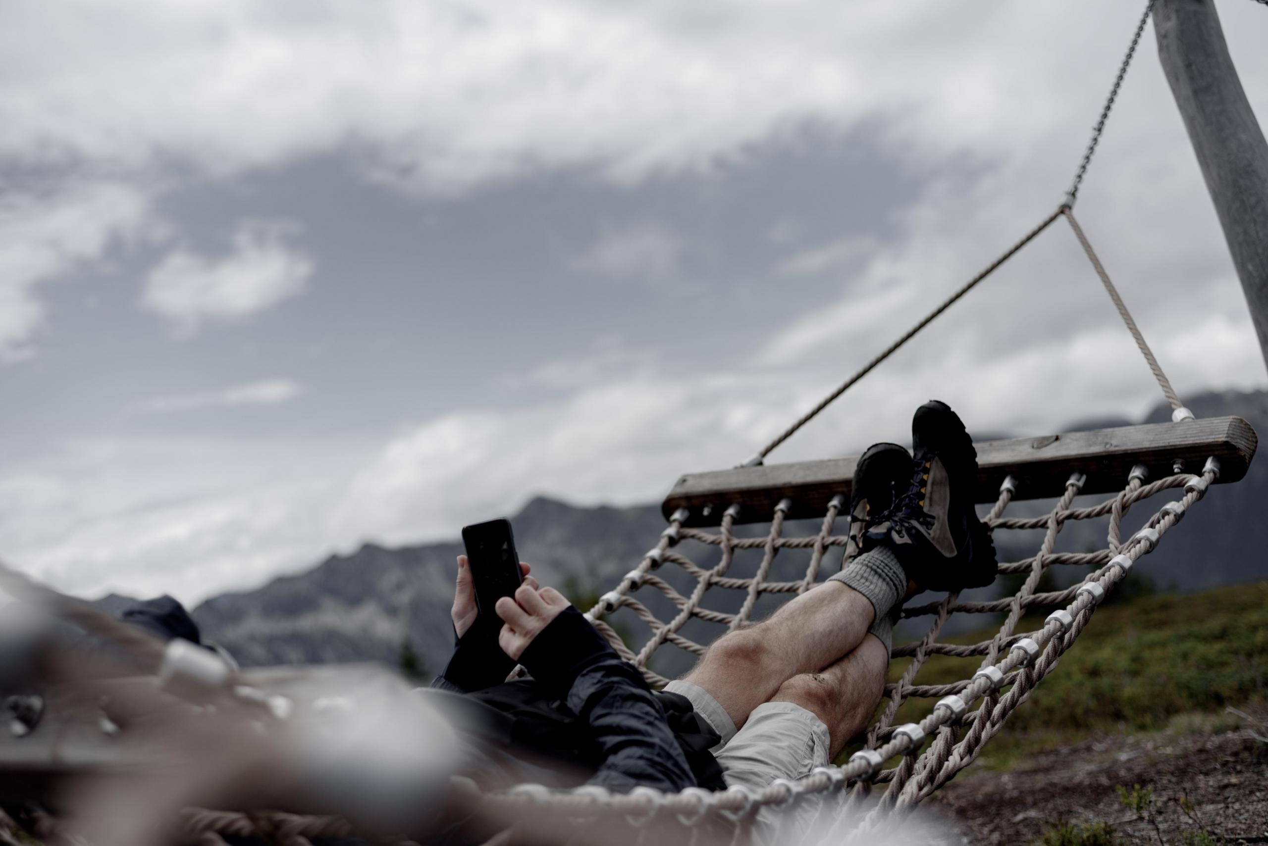 Człowiek leżący na hamaku z telefonem w dłoni.