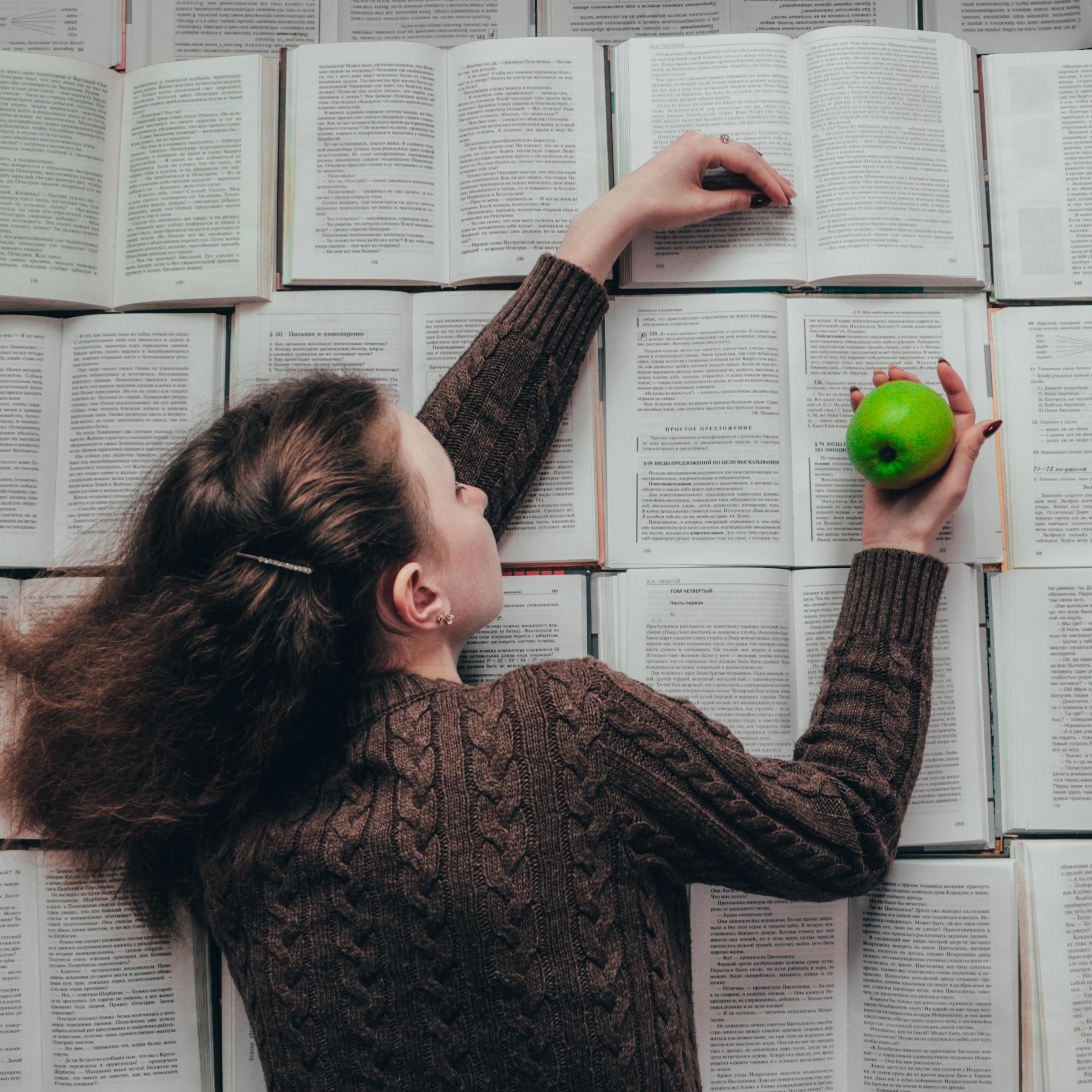 Dziewczyna leżąca na książkach z zielonym jabłkiem w dłoni.