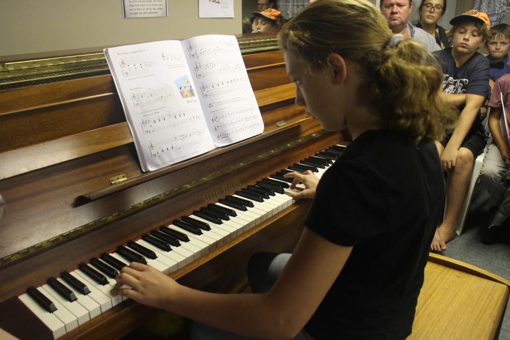 dziewczynka grająca na pianinie przy małej publiczności w klasie