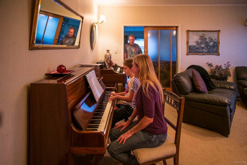 kobieta z dzieckiem grający na pianinie i przyglądający się im mężczyzna