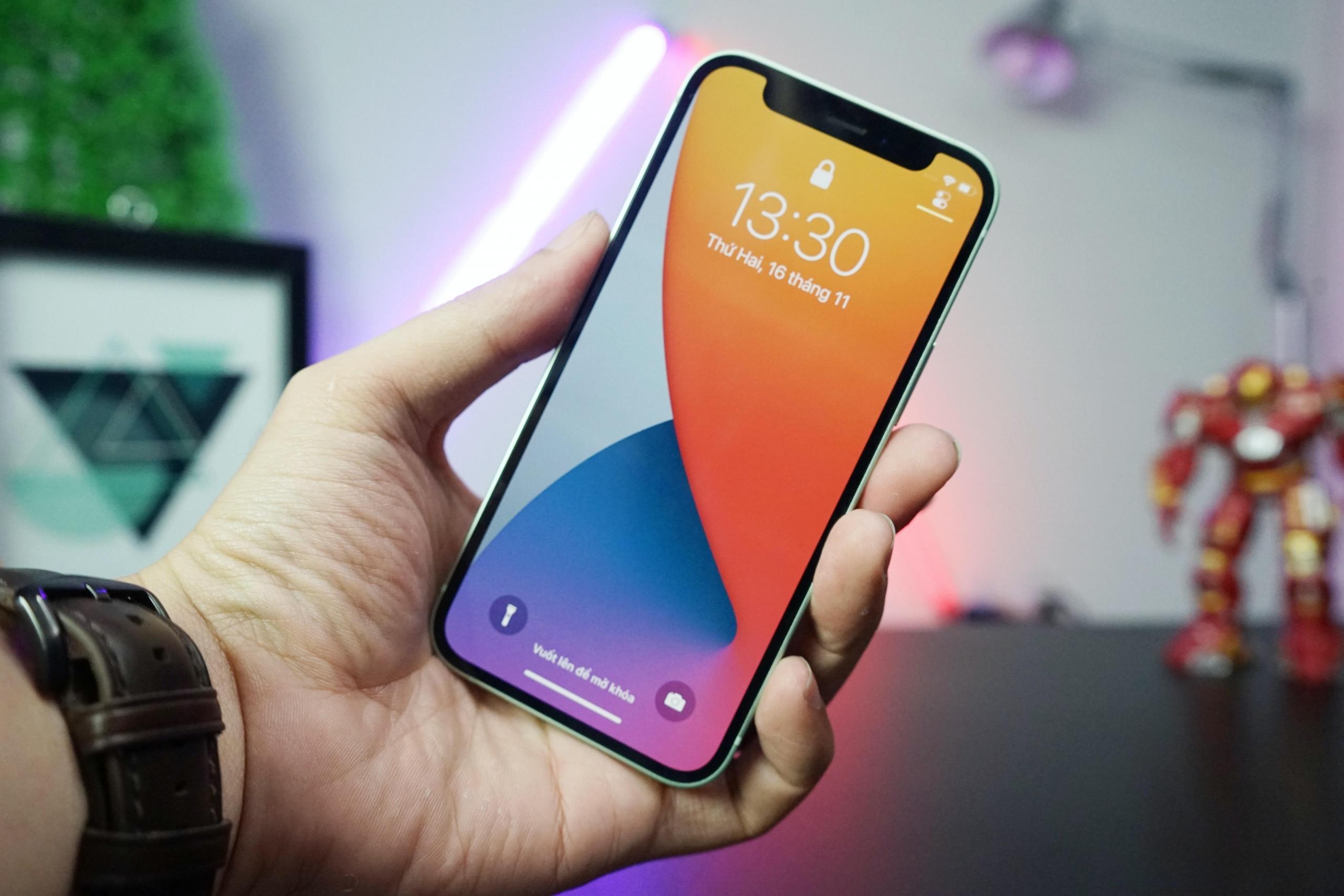 Smartfon w ręku, zegarek na nadgarstku, z komputerem, lampką, robotem zabawką i fioletową świetlówką w tle.