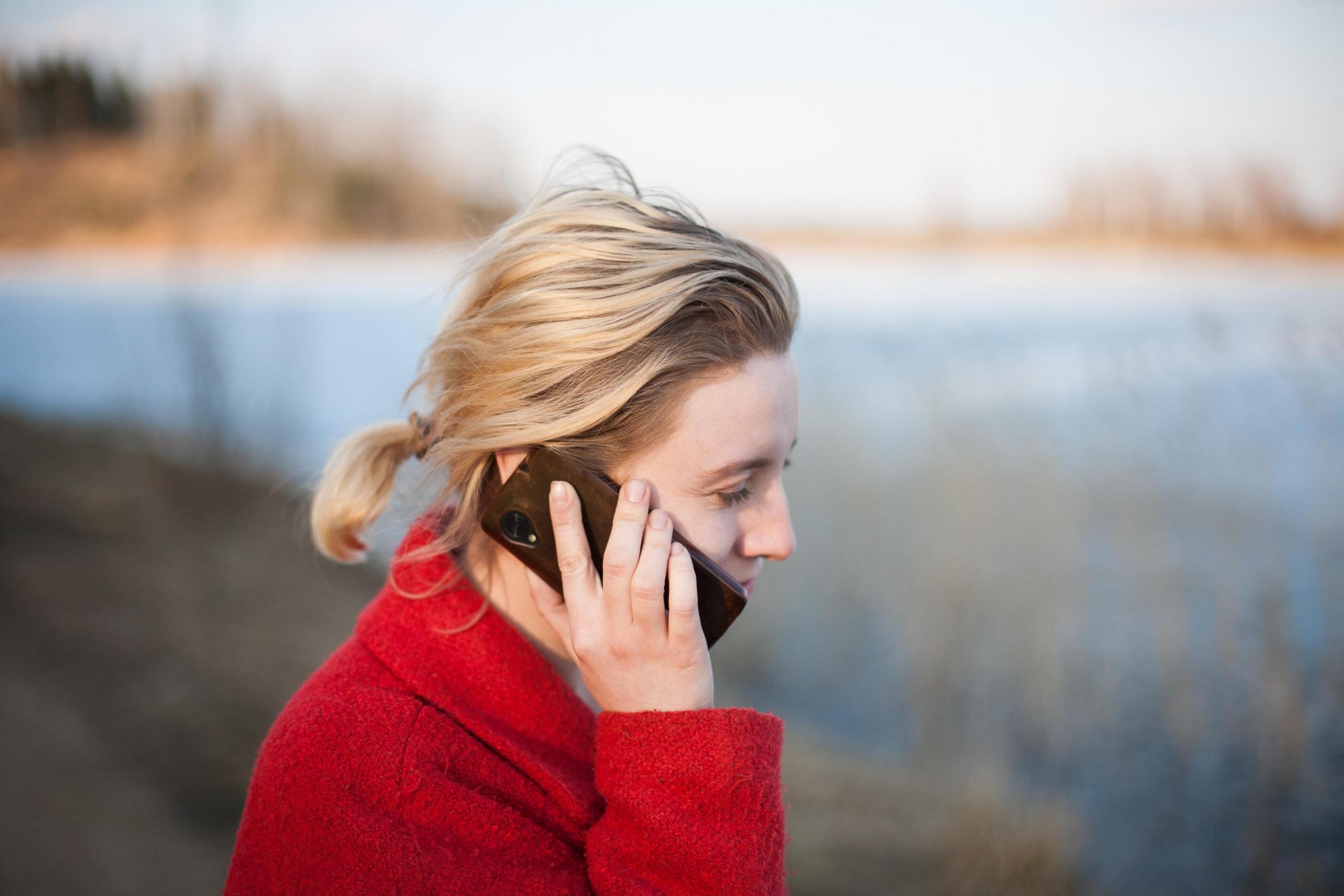 Kobieta w czerwonej kurtce, rozmawiająca przez telefon na zewnątrz.