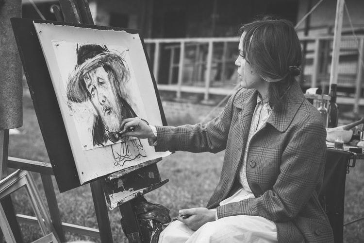 Kobieta w marynarce szkicująca portret mężczyzny w kapeluszu
