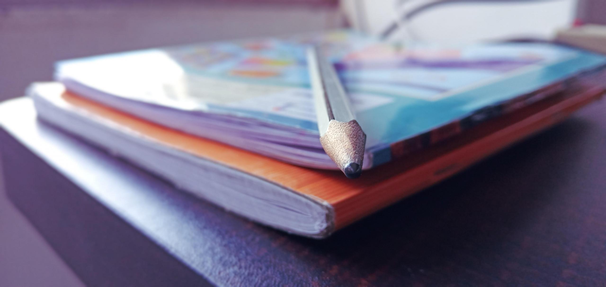 Dwa zeszyty i ołówek na stole.