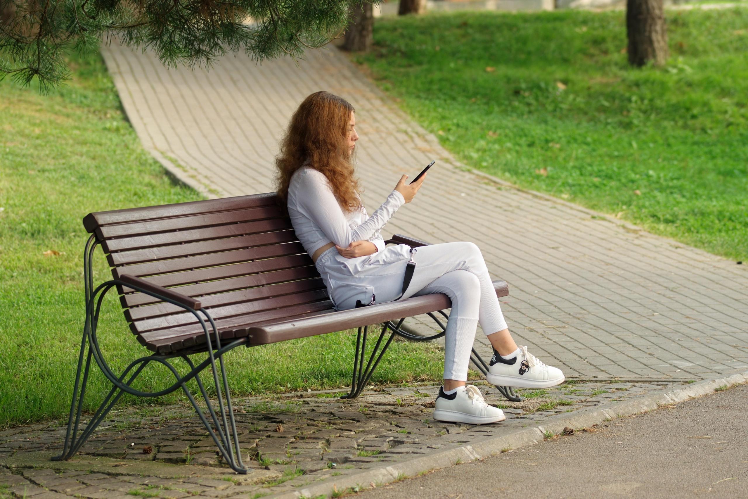 Dziewczyna na ławce z telefonem w ręku.