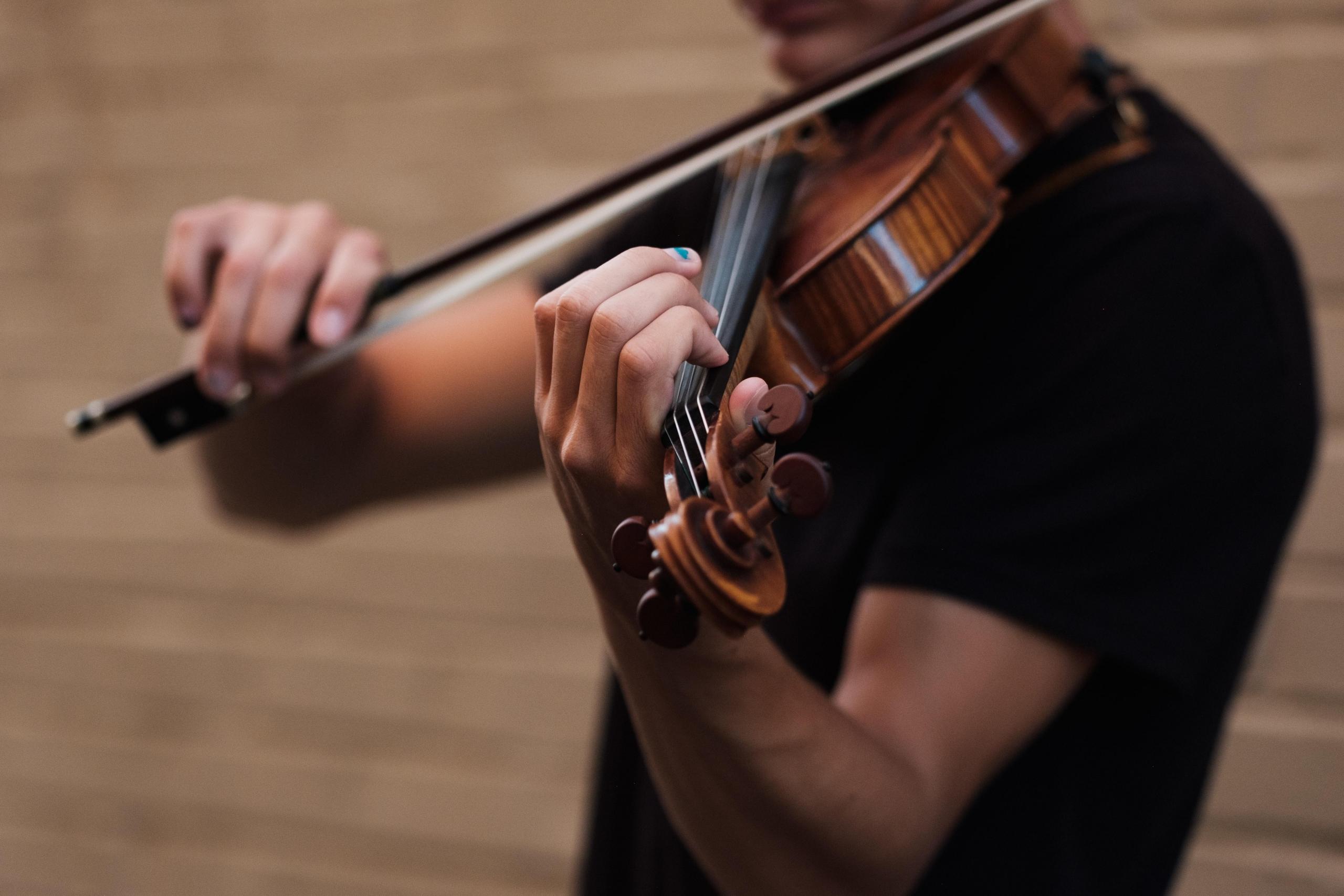 Mężczyzna w czarnej koszulce grający na skrzypkach, instrument smyczkowy, smyczek.