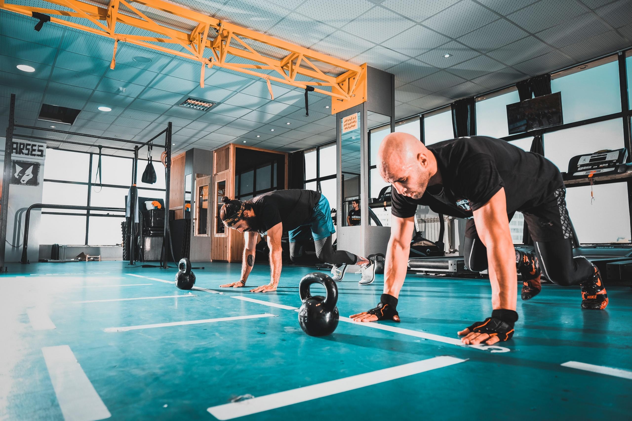 Mężczyźni ćwiczący w siłowni z hantlami kettlebell.