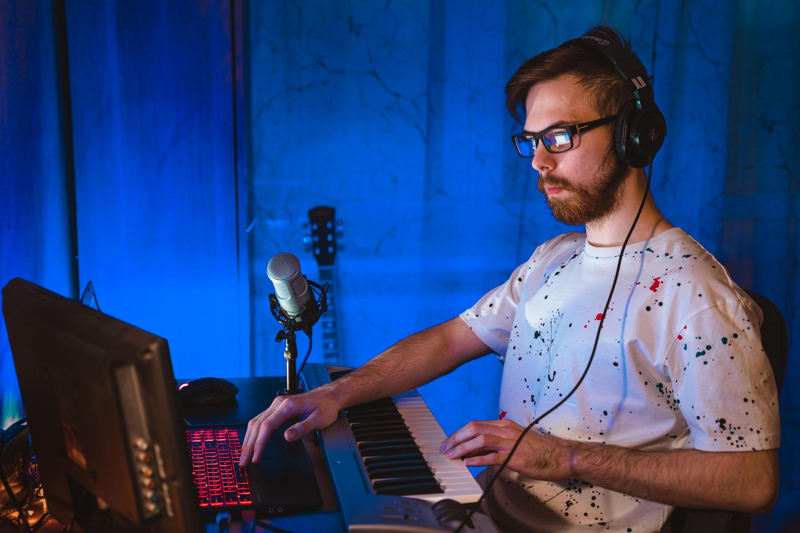 Mężczyzna ze słuchawkami przy keyboardzie i komputerze.