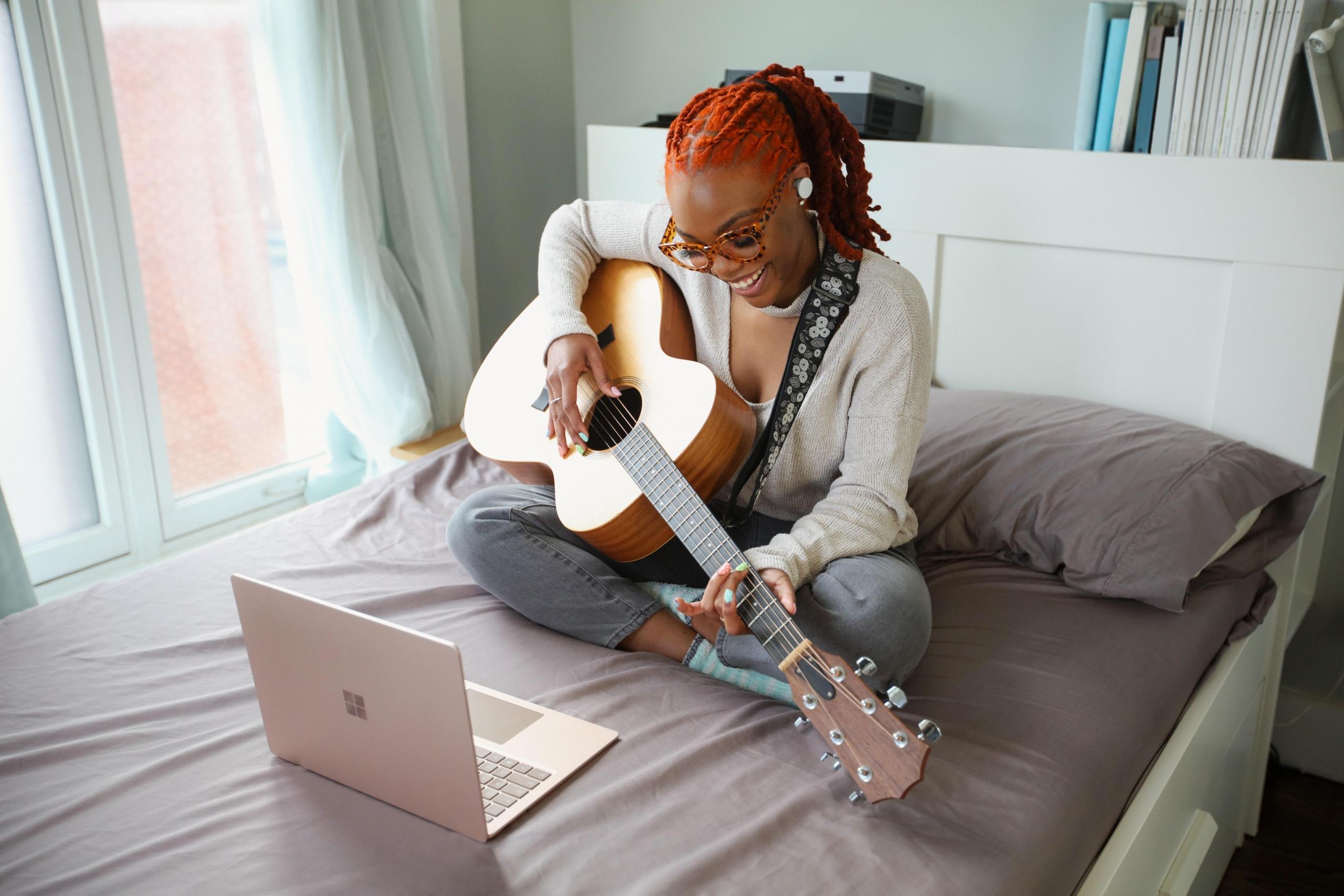 Kobieta przy laptopie grająca na gitarze.
