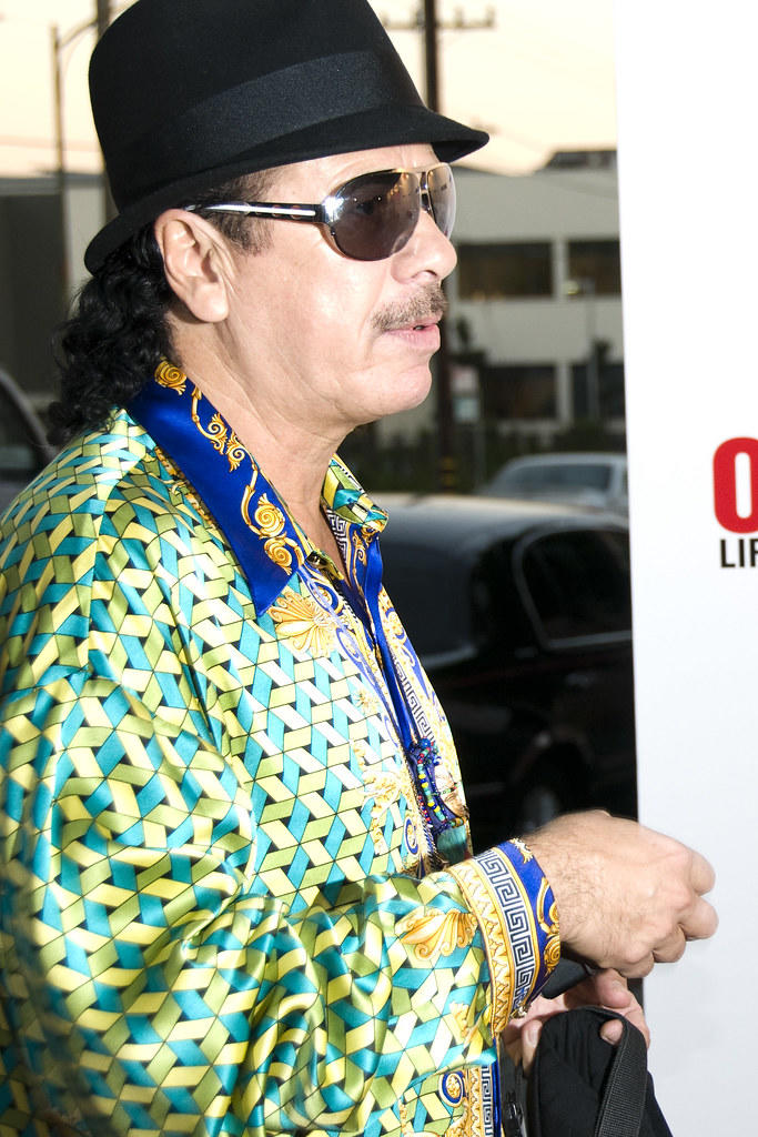 Carlos Santana w zielonej koszuli, okularach przeciwsłonecznych i czarnym kapeluszu.