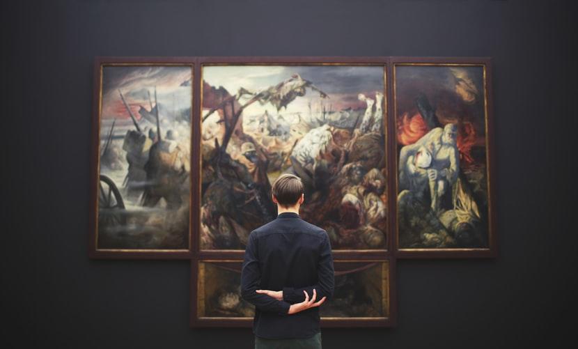Mężczyzna przed zestawem obrazów na czarnej ścianie w muzeum.