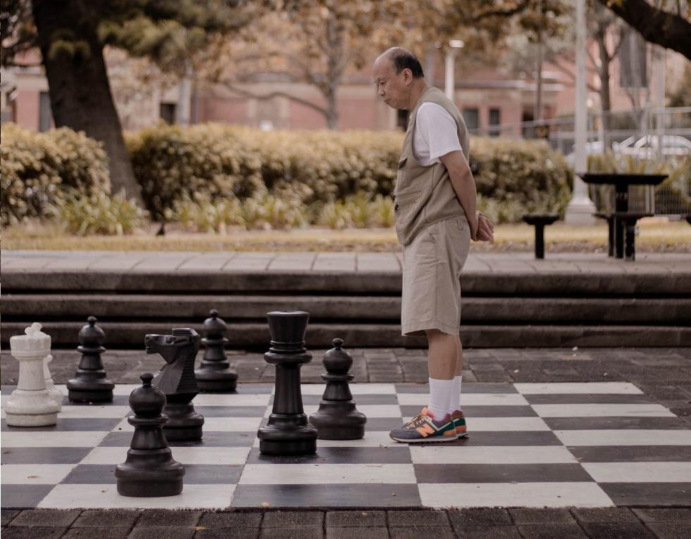 starszy mężczyzna chodzący po dużej szachownicy w parku w jesienny dzień