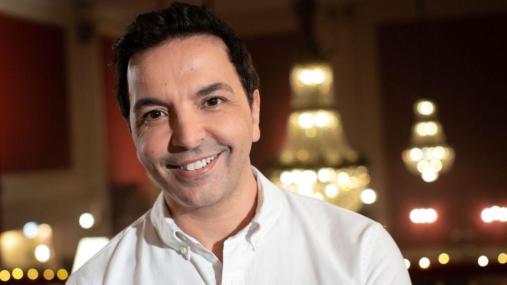 Kamel Ouali w białej koszuli na tle kryształowych żyrandoli