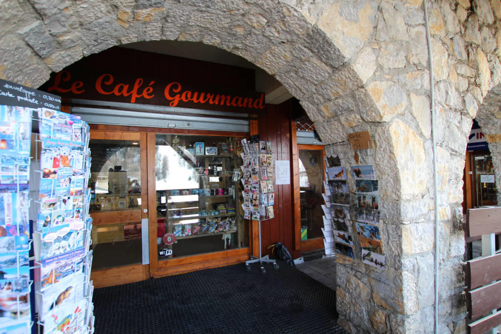 Kawiarnia la cafe gourmand w la plagne we francji, stojak z pocztówkami, wejście do budynku, mur z łukiem.