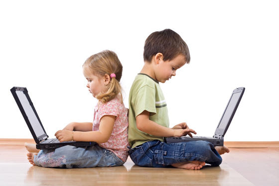 dwoje dzieci siedzących na podłodze plecami do siebie z laptopami na kolanach
