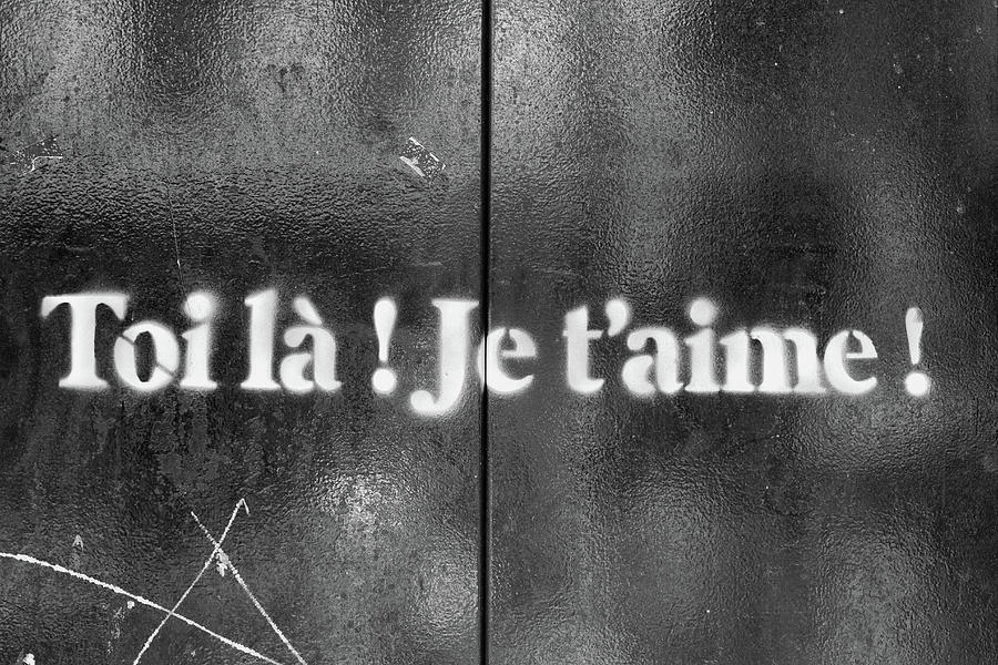Graffiti w formie białego napisu Toi la! Je t'aime! na czarnej ścianie, napis po francusku.