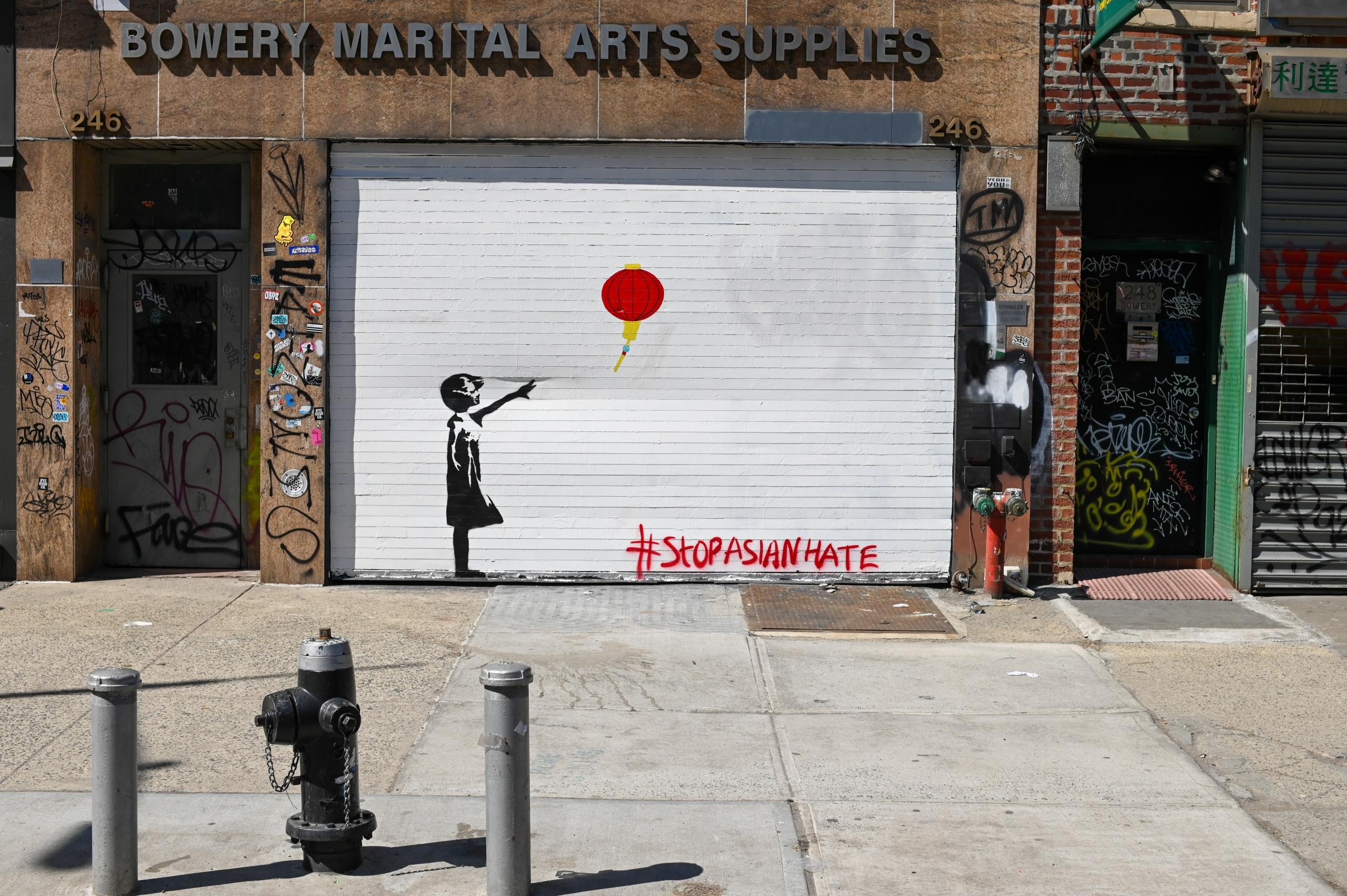 Graffiti Banksy'ego na drzwiach garażowych przestawiające dziewczynkę puszczającą lampion i hashtag z napisem by zaprzestać wrogości w kierunku Azjatów.