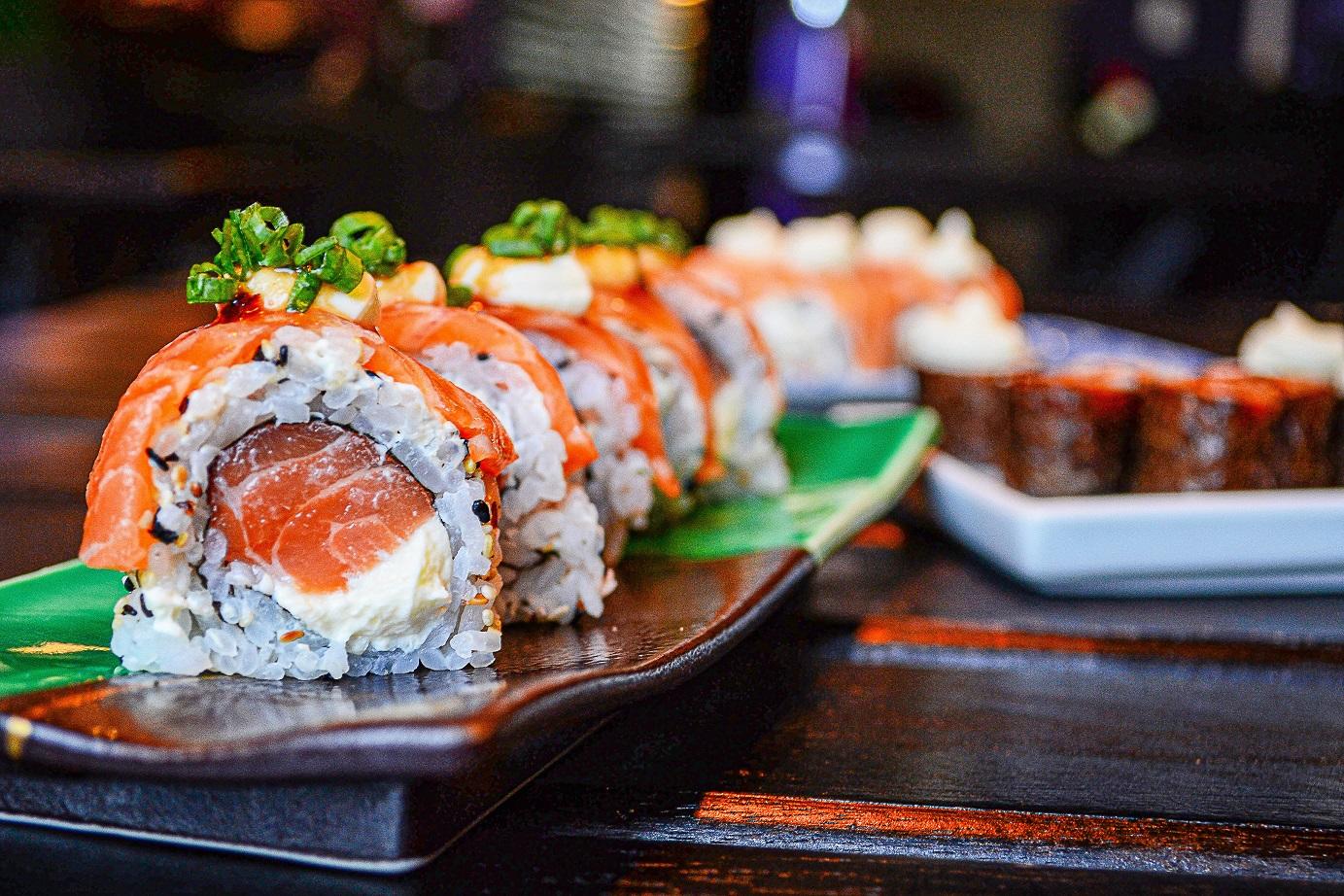 sushi z łososiem poukładane na kolorowym półmisku i w tle na białym talerzu