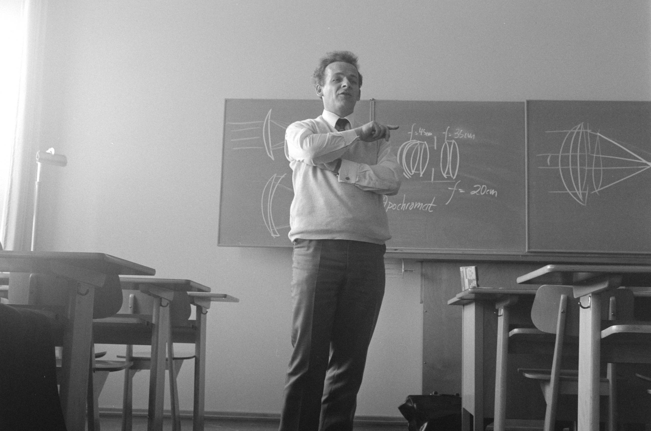 czarno-białe zdjęcie stojącego nauczyciela od matematyki na tle zapisanej tablicy