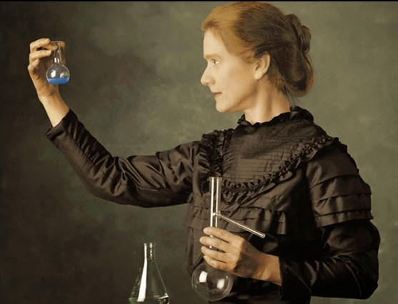 Maria Skłodowska Curie trzyma w dłoniach próbówki chemiczne, szklane naczynia.