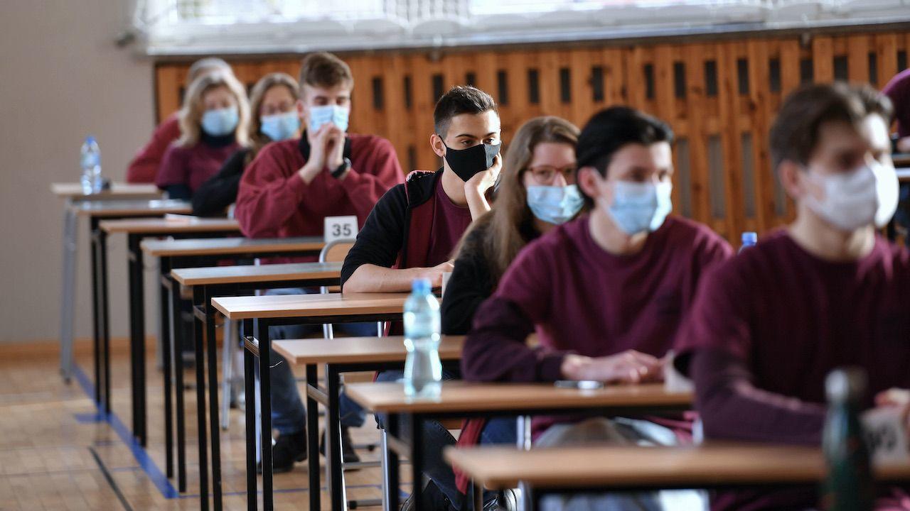 uczniowie w maskach siedzący w ławkach na sali gotowi do pisania egzaminu