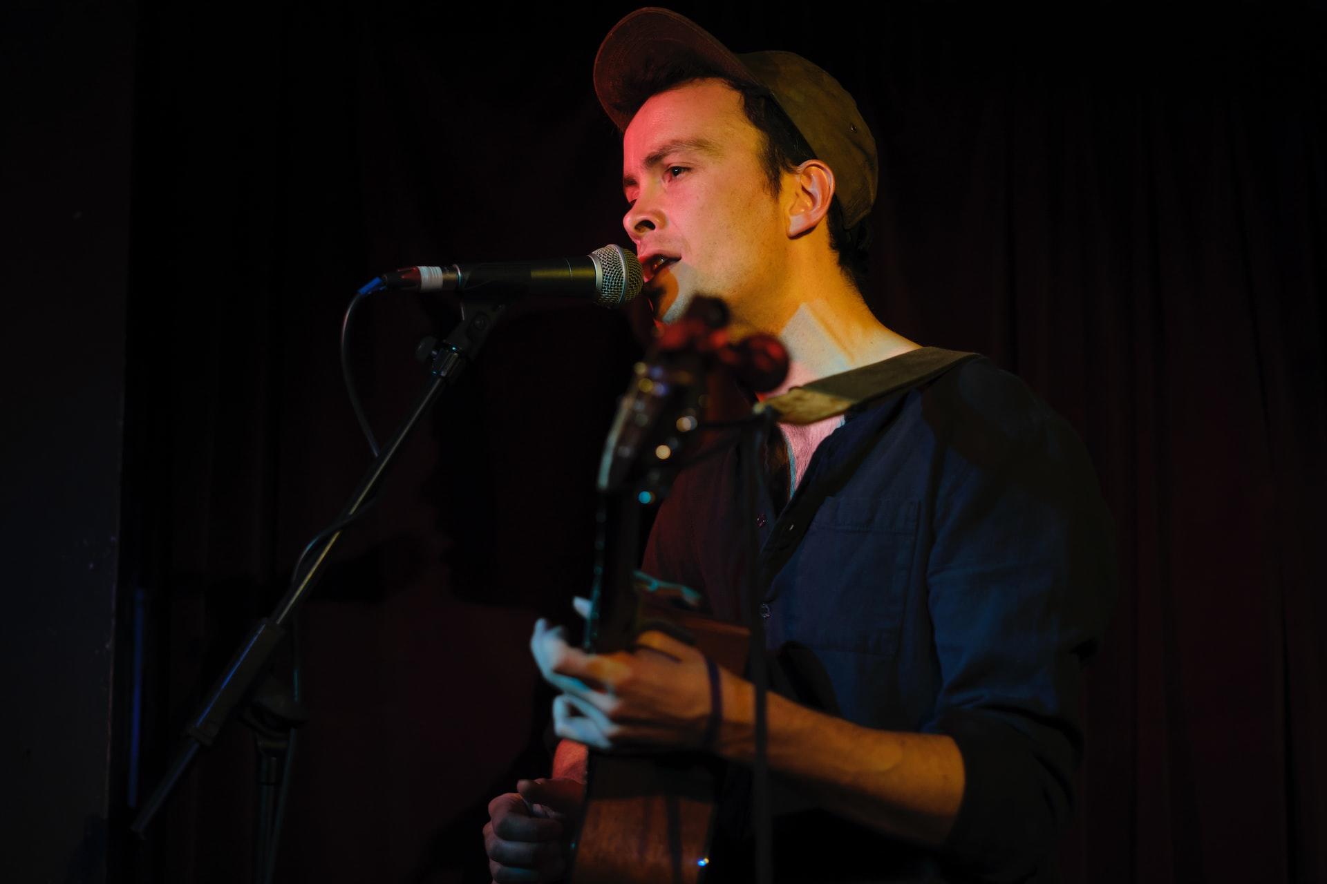 mężczyzna grający na gitarze na scenie z czapką z daszkiem