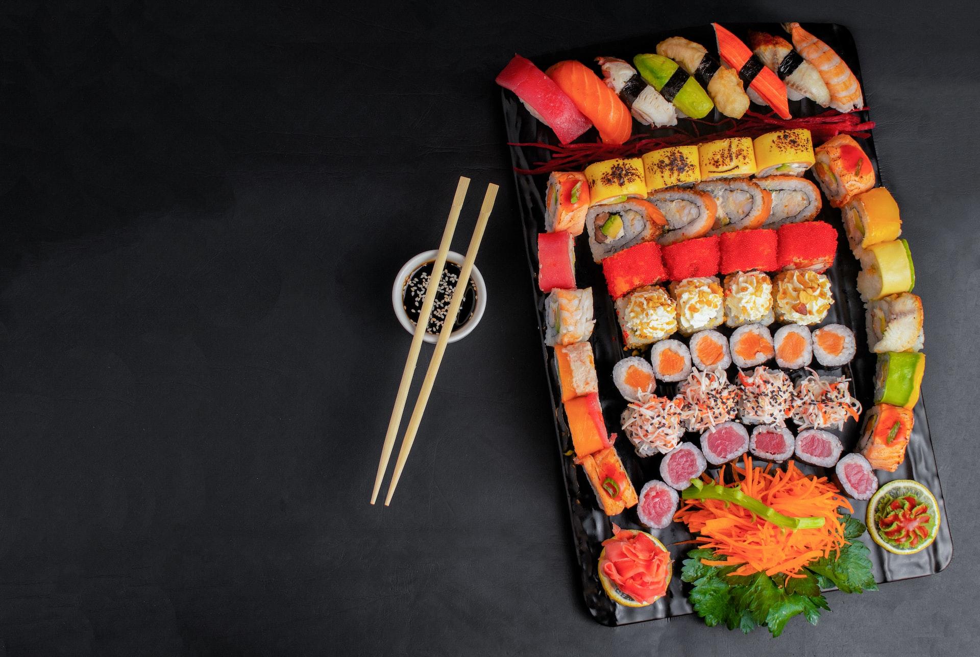 półmisek pelen sushi i pałeczki na małej miseczce z sosem sojowym