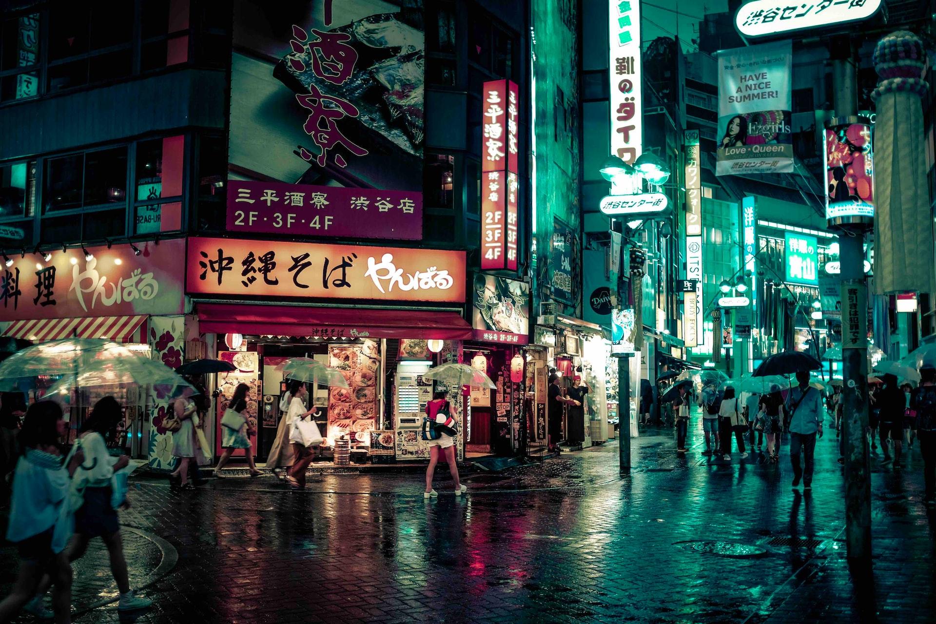 ludzie idący ulicą oświetloną neonami w dzielnicy Shibuya w Tokio